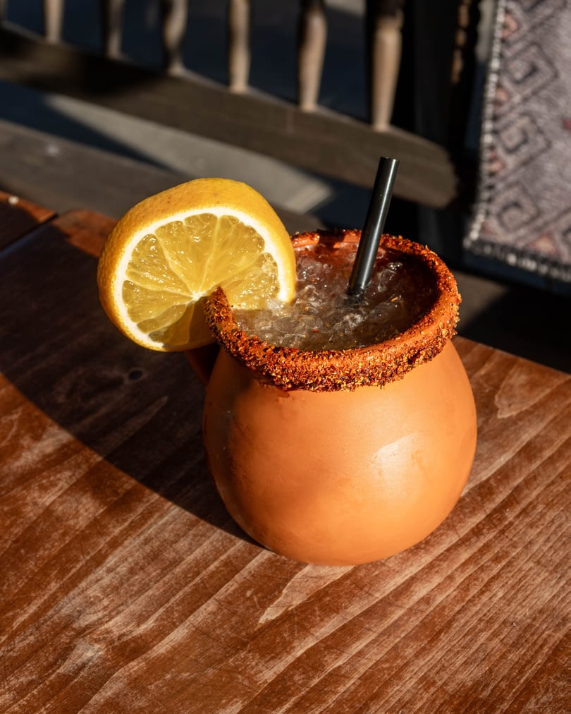 A clay mug with a chili-salted rim, filled with an iced drink and garnished with a lemon slice.